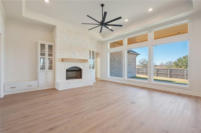 unfurnished living room with a tray ceiling, crown molding, a fireplace, and light wood-type flooring