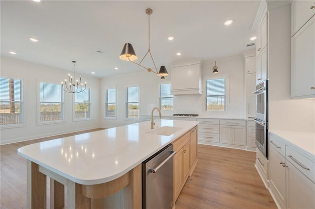 kitchen featuring sink, decorative light fixtures, a large island with sink, stainless steel appliances, and white cabinets