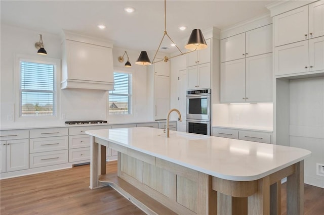 kitchen with white cabinetry, a breakfast bar, double oven, and a center island with sink