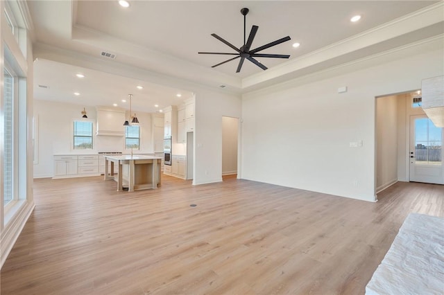 unfurnished living room featuring sink, light wood-type flooring, ornamental molding, a raised ceiling, and ceiling fan