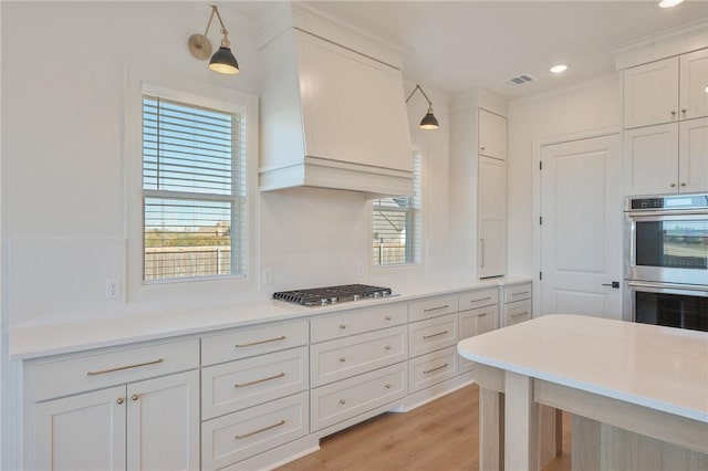 kitchen with pendant lighting, appliances with stainless steel finishes, a wealth of natural light, custom range hood, and white cabinets