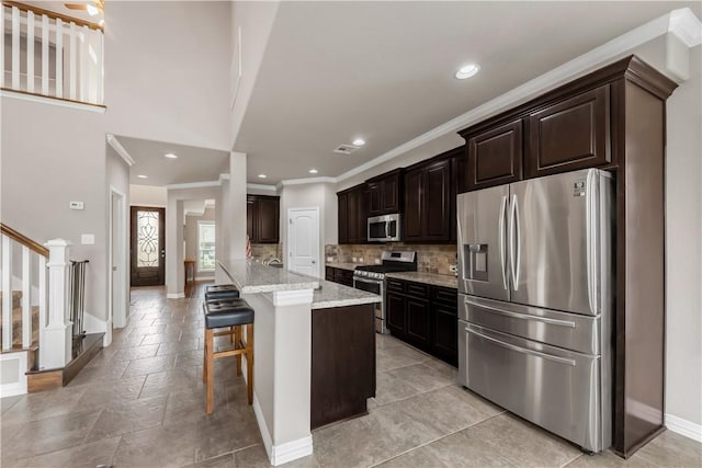 2609 Kimbolton Dr, College Station, TX 77845 - kitchen with stainless steel appliances, crown molding, baseboards, decorative backsplash, and a breakfast bar area