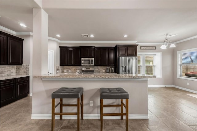 2609 Kimbolton Dr, College Station, TX 77845 - kitchen featuring appliances with stainless steel finishes, a breakfast bar, ornamental molding, decorative backsplash, and a chandelier