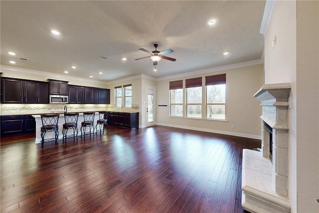 kitchen with a kitchen island with sink, a kitchen breakfast bar, open floor plan, light countertops, and stainless steel microwave