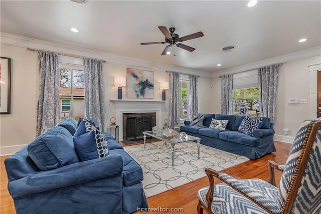 living room featuring a fireplace, hardwood / wood-style flooring, ceiling fan, and crown molding