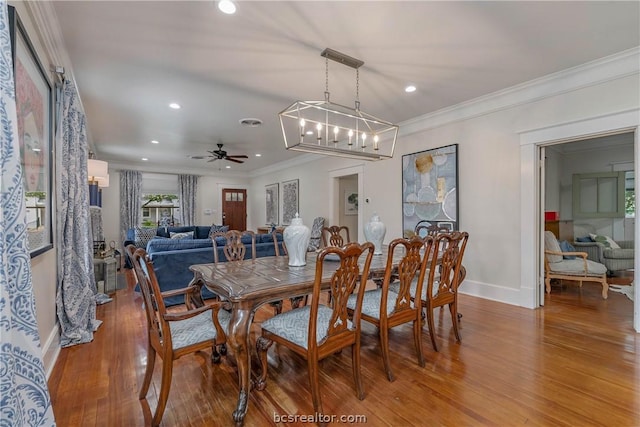 dining area featuring wood-type flooring, ceiling fan with notable chandelier, and crown molding