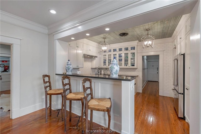 kitchen with decorative light fixtures, white cabinetry, wood-type flooring, stainless steel refrigerator, and a chandelier