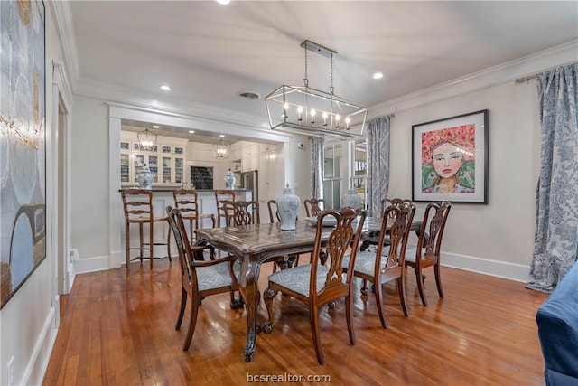 dining area with hardwood / wood-style floors, crown molding, and an inviting chandelier