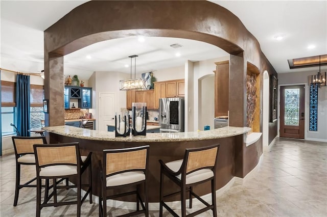 25603 Muirfield Bend Ct, Spring, TX 77389 - kitchen with arched walkways, stainless steel fridge, a chandelier, light stone countertops, and recessed lighting