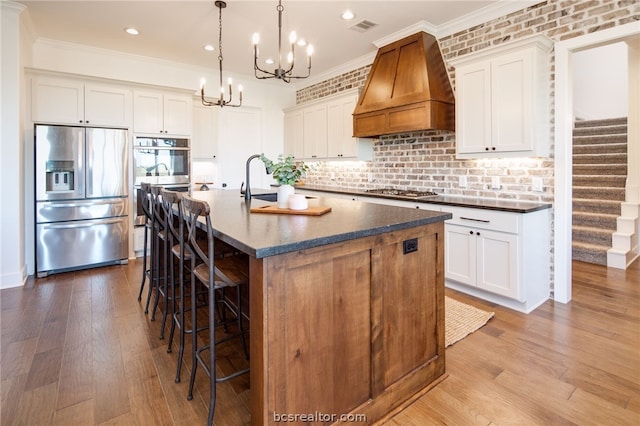 kitchen featuring a kitchen island with sink, white cabinetry, custom exhaust hood, and appliances with stainless steel finishes