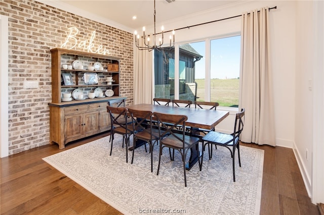 dining space featuring dark hardwood / wood-style floors, ornamental molding, brick wall, and an inviting chandelier