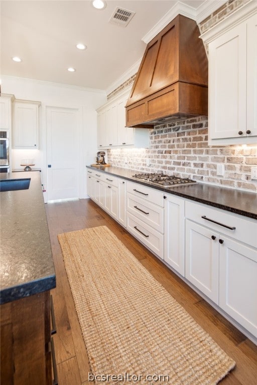 kitchen with ornamental molding, custom range hood, stainless steel gas cooktop, hardwood / wood-style floors, and white cabinetry