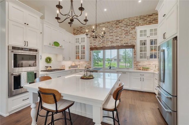 5026 Yellow Tanager Ct, College Station, TX 77845 - kitchen with stainless steel appliances, a chandelier, light countertops, white cabinets, and brick wall