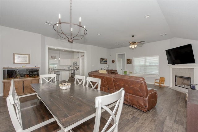 dining space featuring a tiled fireplace, lofted ceiling, hardwood / wood-style floors, and ceiling fan with notable chandelier