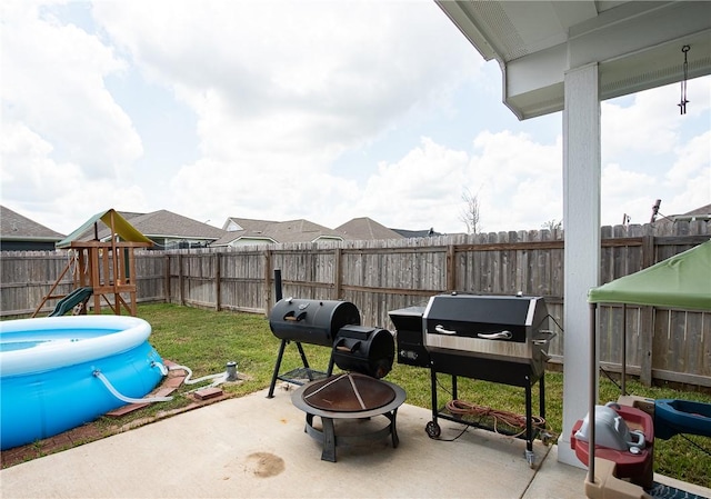 view of patio featuring a playground, area for grilling, a fire pit, and a fenced in pool