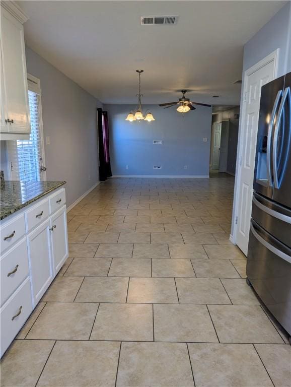 kitchen with stainless steel refrigerator with ice dispenser, light tile patterned flooring, dark stone countertops, ceiling fan with notable chandelier, and white cabinets