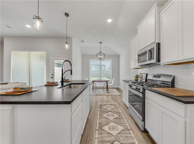 kitchen with white cabinetry, hanging light fixtures, stainless steel appliances, and a center island with sink