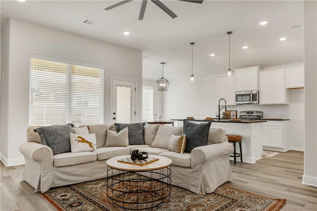 living room featuring ceiling fan, sink, and light hardwood / wood-style floors