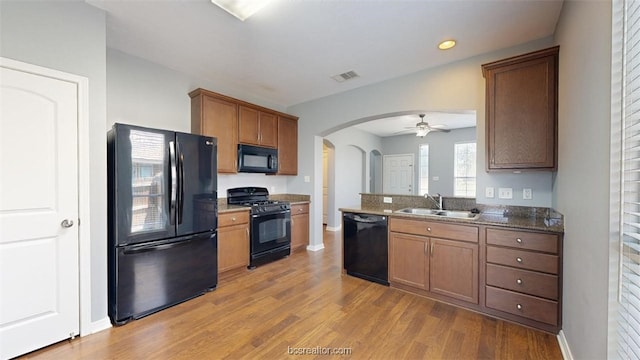 kitchen with sink, ceiling fan, light hardwood / wood-style floors, dark stone counters, and black appliances