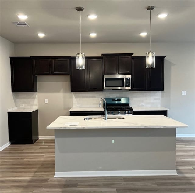 kitchen featuring stainless steel appliances, a kitchen island with sink, and decorative light fixtures