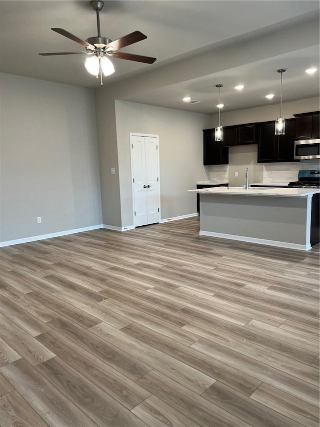 kitchen featuring appliances with stainless steel finishes, sink, hanging light fixtures, a center island with sink, and light wood-type flooring