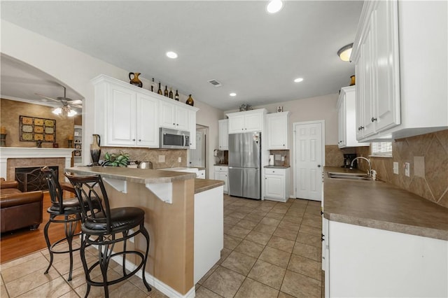 kitchen with white cabinets, sink, appliances with stainless steel finishes, a kitchen bar, and kitchen peninsula