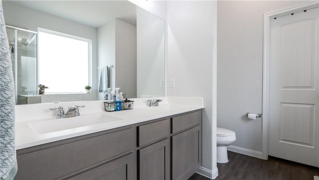 full bathroom with wood finished floors, double vanity, a stall shower, a sink, and toilet