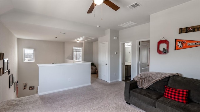 living area with light carpet, visible vents, attic access, and a ceiling fan