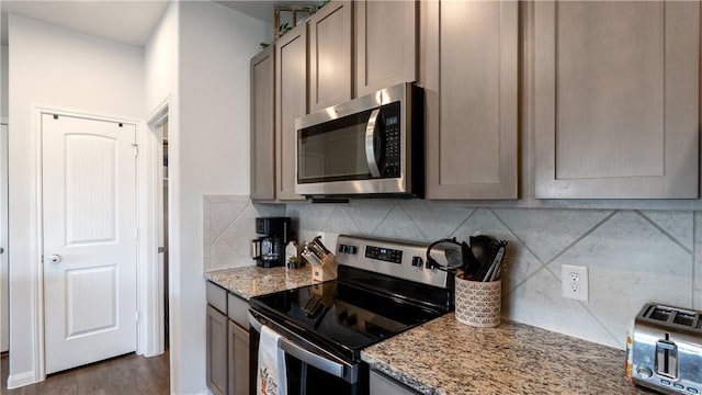 kitchen featuring light stone countertops, backsplash, appliances with stainless steel finishes, and dark wood-type flooring