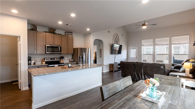 kitchen featuring visible vents, arched walkways, stainless steel appliances, a ceiling fan, and a kitchen island with sink