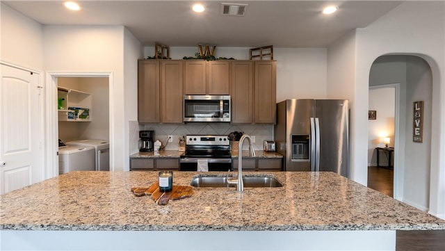 kitchen featuring a sink, arched walkways, appliances with stainless steel finishes, decorative backsplash, and washing machine and clothes dryer