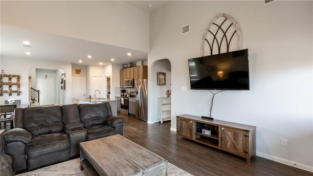 living room featuring visible vents, arched walkways, baseboards, and dark wood finished floors