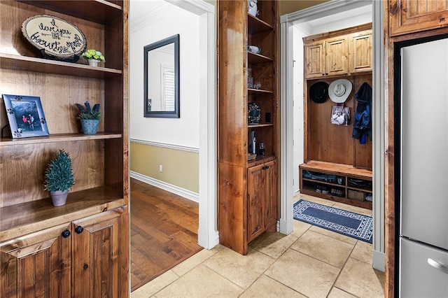 mudroom with built in features, crown molding, baseboards, and light tile patterned floors