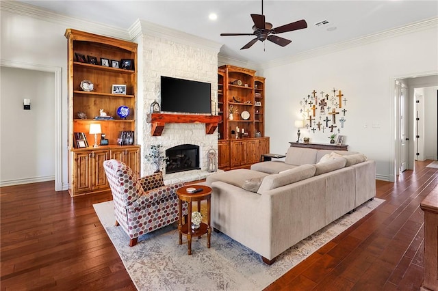 living area featuring baseboards, ceiling fan, ornamental molding, dark wood-type flooring, and a stone fireplace