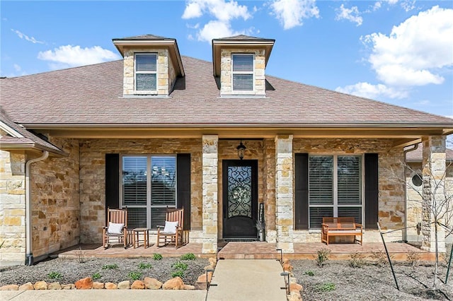 property entrance featuring covered porch, a shingled roof, and stone siding