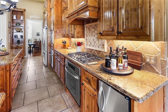 kitchen with brown cabinetry, custom range hood, stainless steel appliances, and decorative backsplash