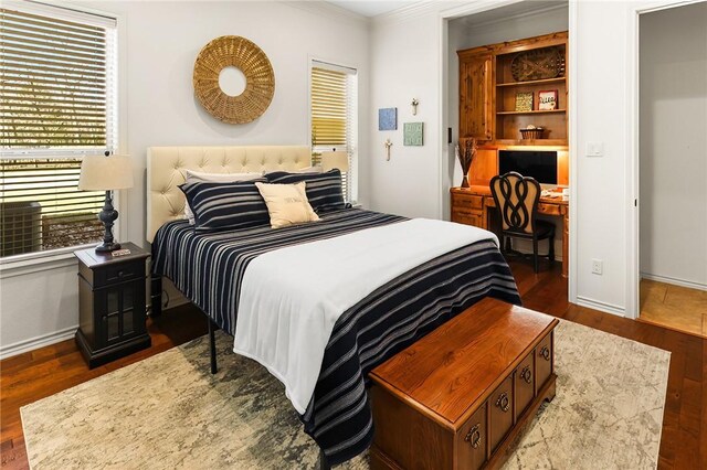 bedroom featuring built in study area, crown molding, baseboards, and wood finished floors