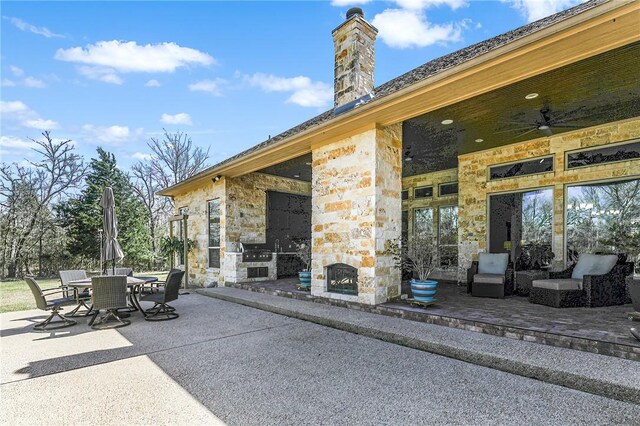 view of patio with ceiling fan, outdoor dining space, and an outdoor stone fireplace