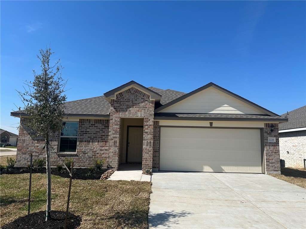 single story home featuring a garage, driveway, a shingled roof, brick siding, and a front yard