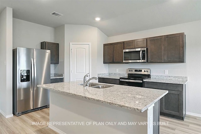 103 Comal Dr, Huntsville, TX 77340 - kitchen featuring stainless steel appliances, light wood finished floors, dark brown cabinetry, light stone countertops, and vaulted ceiling