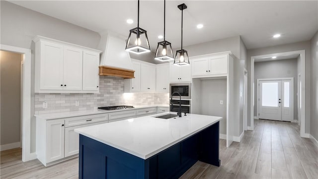 kitchen featuring built in microwave, a kitchen island with sink, white cabinets, and decorative light fixtures