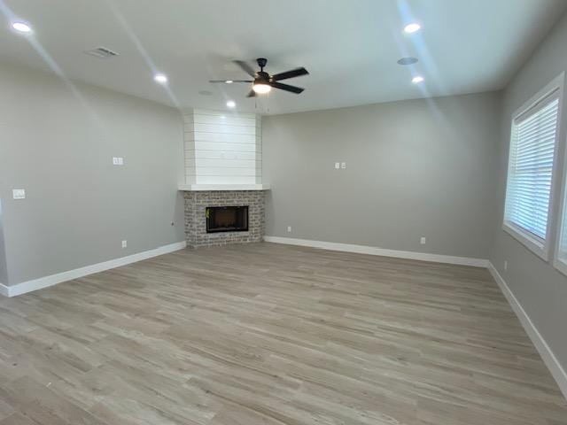 unfurnished living room with ceiling fan, a fireplace, and light hardwood / wood-style flooring