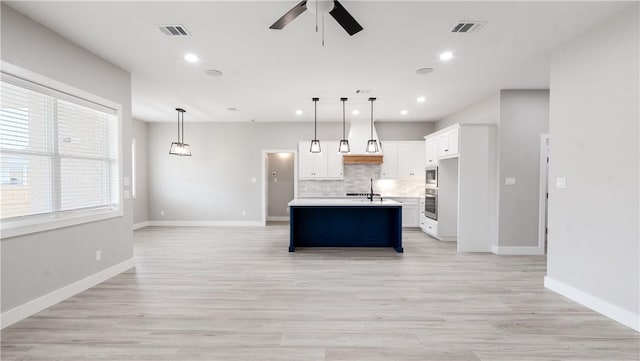 kitchen featuring hanging light fixtures, a kitchen island with sink, white cabinets, light hardwood / wood-style floors, and backsplash