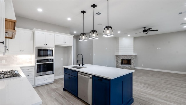 kitchen with hanging light fixtures, white cabinetry, appliances with stainless steel finishes, and a kitchen island with sink