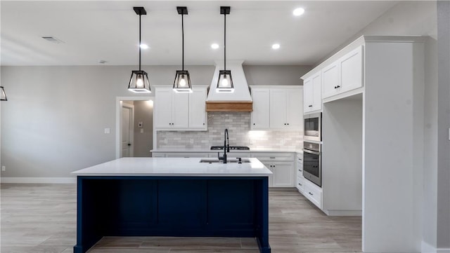 kitchen with hanging light fixtures, white cabinetry, appliances with stainless steel finishes, and a center island with sink