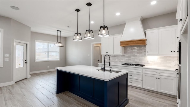 kitchen featuring pendant lighting, a kitchen island with sink, custom range hood, and white cabinets