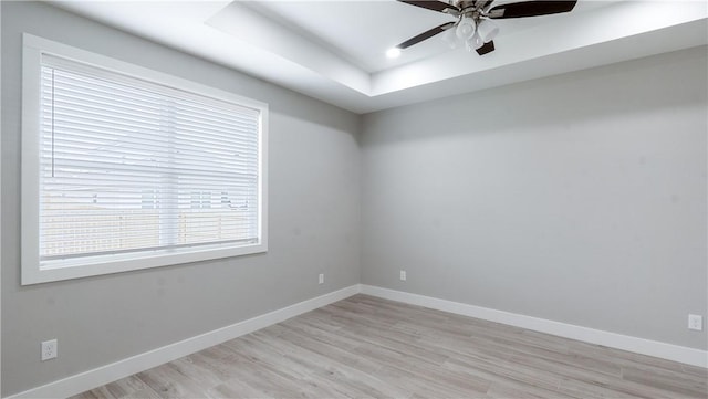 spare room with a tray ceiling, ceiling fan, and light wood-type flooring