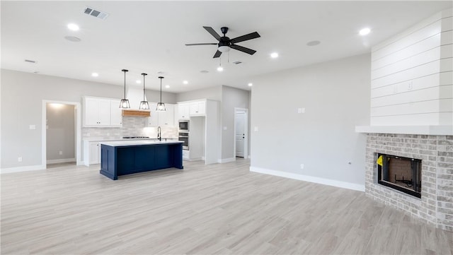 kitchen featuring white cabinetry, hanging light fixtures, a brick fireplace, a center island with sink, and light hardwood / wood-style flooring