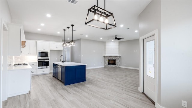 kitchen featuring appliances with stainless steel finishes, pendant lighting, white cabinets, a kitchen island with sink, and blue cabinetry