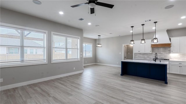 kitchen featuring pendant lighting, white cabinetry, tasteful backsplash, light hardwood / wood-style floors, and a center island with sink